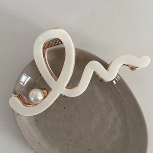 Macro detail of wave-shaped acetate hair claw with gold base and pearl accent