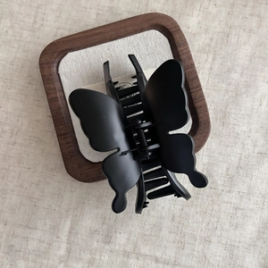 Detailed close-up of a matte black butterfly hair claw clip on a minimalist linen background