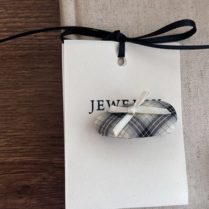 Detail of checkered oval hair clip with white ribbon bow on jewelry display card
