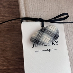 Close-up of blue plaid oval hair clip with black ribbon on jewelry card packaging