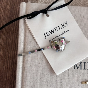 Détail de la barrette en métal argenté avec cœur à pois colorés sur carte bijoux