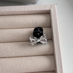 Détail d'une pince à cheveux noire avec nœud en cristal et perle sur velours beige