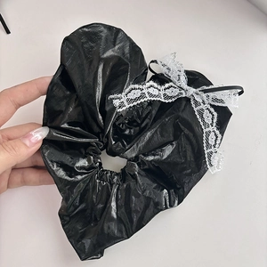 Large black leather-textured scrunchie with a white lace bow in a chic handheld shot