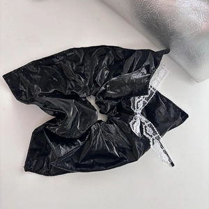 Detail of a large black glossy faux leather scrunchie with a white lace bow accent