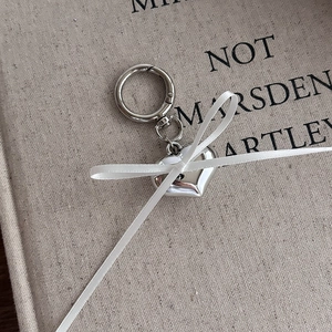 Close-up of polished silver heart pendant with white ribbon and spring clasp on linen