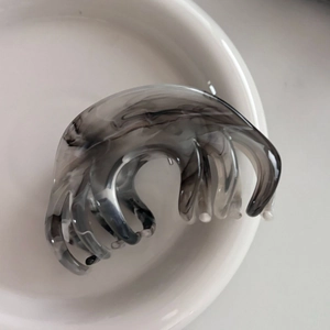 Macro detail of ink marble pattern hair claw clip on white minimalist background