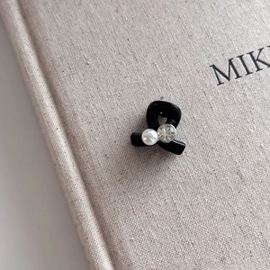 Détail d'une mini pince à cheveux noire avec perle et cristal sur un livre texturé