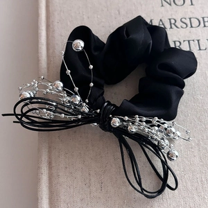 Détail d'un chouchou en satin noir avec frange de perles argentées sur un livre en lin
