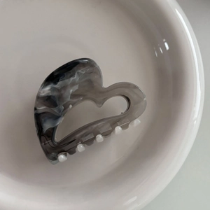 Detail of heart-shaped marble grey hair claw clip on a minimalist white ceramic plate