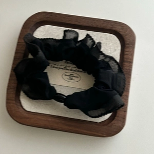 Elegant black ruffle mesh scrunchie with pearl detail on a minimal wooden tray