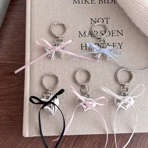 Silver bow and heart pendant keychains with colorful ribbons on a book surface