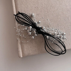 Détail de la pince à cheveux noeud avec perles argentées sur fond de livre en lin
