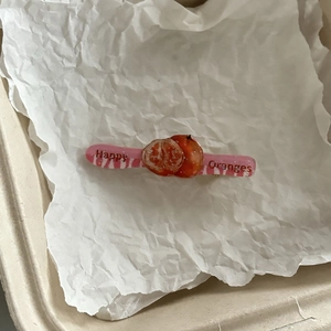 Detail van een zoete fruithaarspeld met 3D-sinaasappels en Happy Oranges tekst