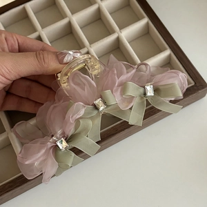 Dettaglio di fermaglio per capelli in organza rosa con fiocchi verdi e cristalli