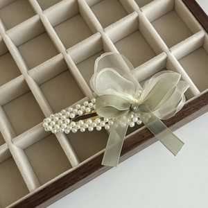 Dettaglio di un elegante fermaglio per capelli in perle con fiocco verde e tulle