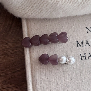 Detalle de cuentas de resina de corazón púrpura y perlas blancas en clips plateados