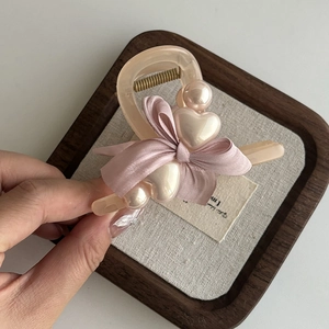 Details der rosa Schleifen-Haarklammer mit glänzenden Perlen und Herz auf Goldfeder