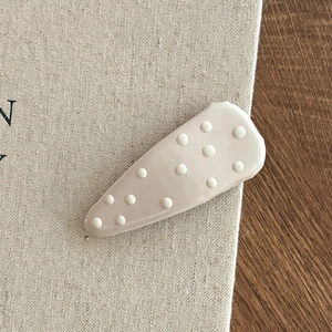 Fermaglio beige a goccia con pois bianchi 3D su sfondo di lino minimalista