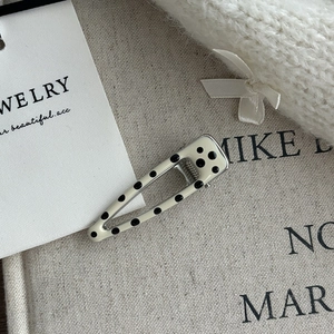 Detailed close-up of cream BB hair clip with black polka dots and metal base