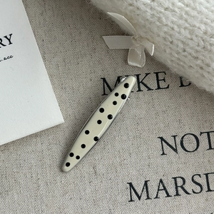 Detailed macro view of the polka dot enamel hair clip on a minimalist textured background