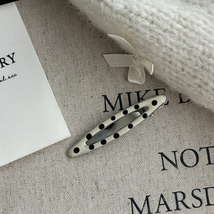 Close-up of spindle-shaped hair clip with black polka dots on creamy white metal enamel