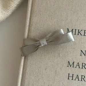 Makroaufnahme einer silbernen Satinschleifen-Haarspange mit seidigem Glanz auf Buch