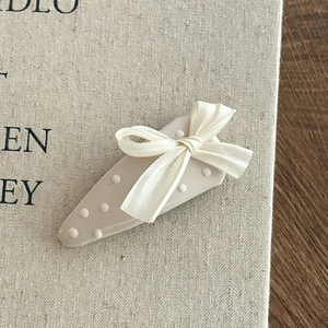 Dettaglio del fermaglio blu a pois con fiocco in seta crema e finitura strutturata