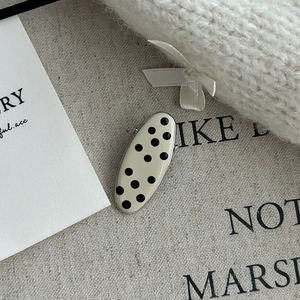 Close-up of vintage black and white polka dot metal hair clip with gold border