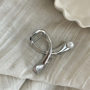 Gros plan d'une pince à cheveux argentée avec perle blanche sur un tissu en lin beige