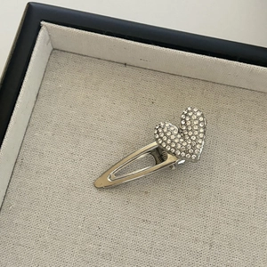 Detail of silver heart hair clip with white rhinestones on a beige jewelry display