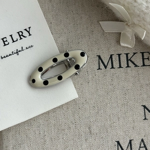 Detailed macro view of an oval black and white polka dot enamel hair clip with metal base