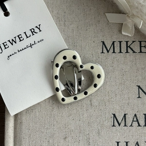 Close-up of heart-shaped hair clip with black polka dots and silver metal duckbill clip