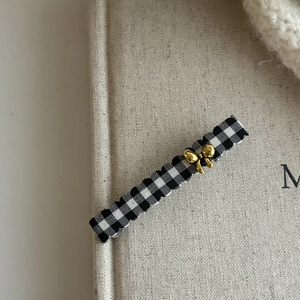Detail of checkered hair clip with gold bow and elegant scalloped edges on fabric