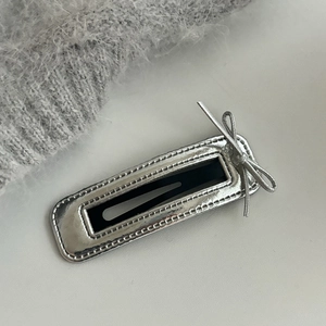 Close-up of a silver rectangular metal hair clip featuring a small bow and textured edges