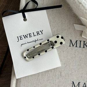Detailed close-up of cream rectangular hair clip with black polka dots on a metal base