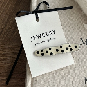 Detailed macro shot of a cream-white hair clip with black polka dots on a metal base