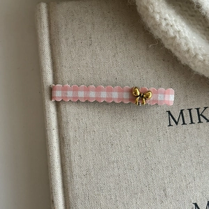 Close-up of pink plaid fabric hair clip with a gold bow on a vintage book surface