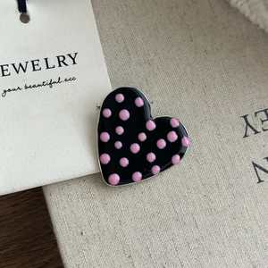 Détail d'une épingle à cheveux cœur en métal émaillé noir avec des pois roses