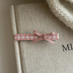 Detailed view of pink plaid ribbon bow hair clip on cozy beige textured background