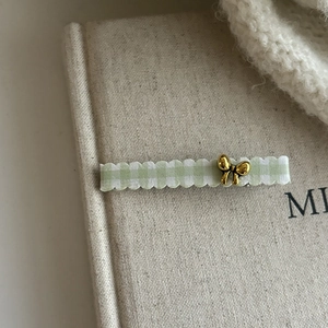 Detail view of a green gingham checkered hair clip with a metallic gold bow accessory