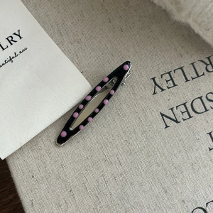 Détail de la pince à cheveux Y2K en métal à pois noirs et roses sur fond de tissu