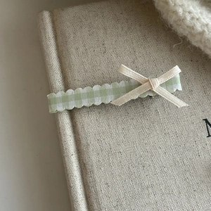 Detailed close-up of a green plaid ribbon hair clip with a bow on a creamy canvas backdrop