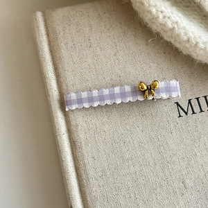 Detailed shot of purple plaid hair clip with gold bow on a beige book background