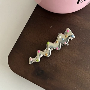 Détail de pince à cheveux argentée ondulée avec des pois 3D colorés sur bois