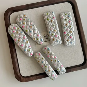 Detail of five silver hair clips with colorful dots and quilted texture on a wooden tray