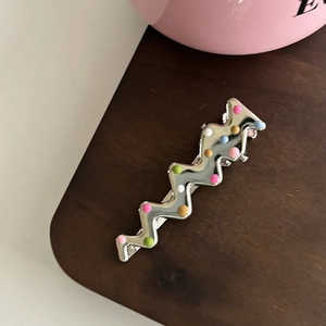 Détail de la pince à cheveux argentée ondulée avec des pois en émail coloré sur bois