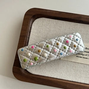 Close-up of silver quilted hair clip with colorful 3D dots on a wooden tray