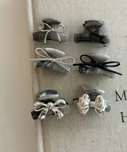 Detailed view of six mini marble texture hair claws with silver bow accents on textured background