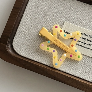 Detail of yellow star hair clip with colorful dots on a rustic beige linen background