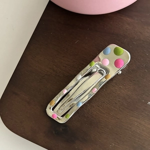 Pince à cheveux en métal argenté avec des pois colorés sur un fond de bois naturel